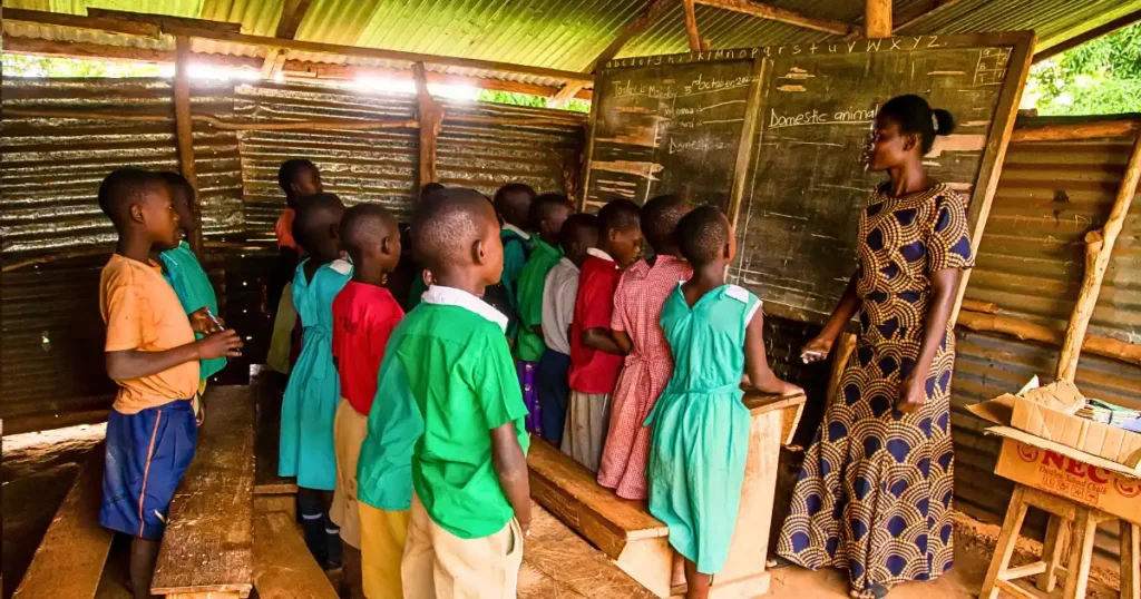 A group of rural Ugandan students sit in a modest classroom as their teacher instructs them. The worn desks, simple materials, and sparse surroundings reveal the challenges of limited resources, while the attentive faces of the pupils reflect curiosity, determination, and the transformative power of education.