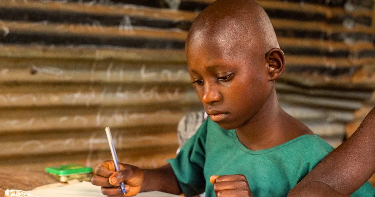 A young girl in a rural Ugandan classroom takes notes with quiet determination, surrounded by a run-down learning environment that reflects both the hardship and hope driving Baino Social Impact’s mission to empower children through education.