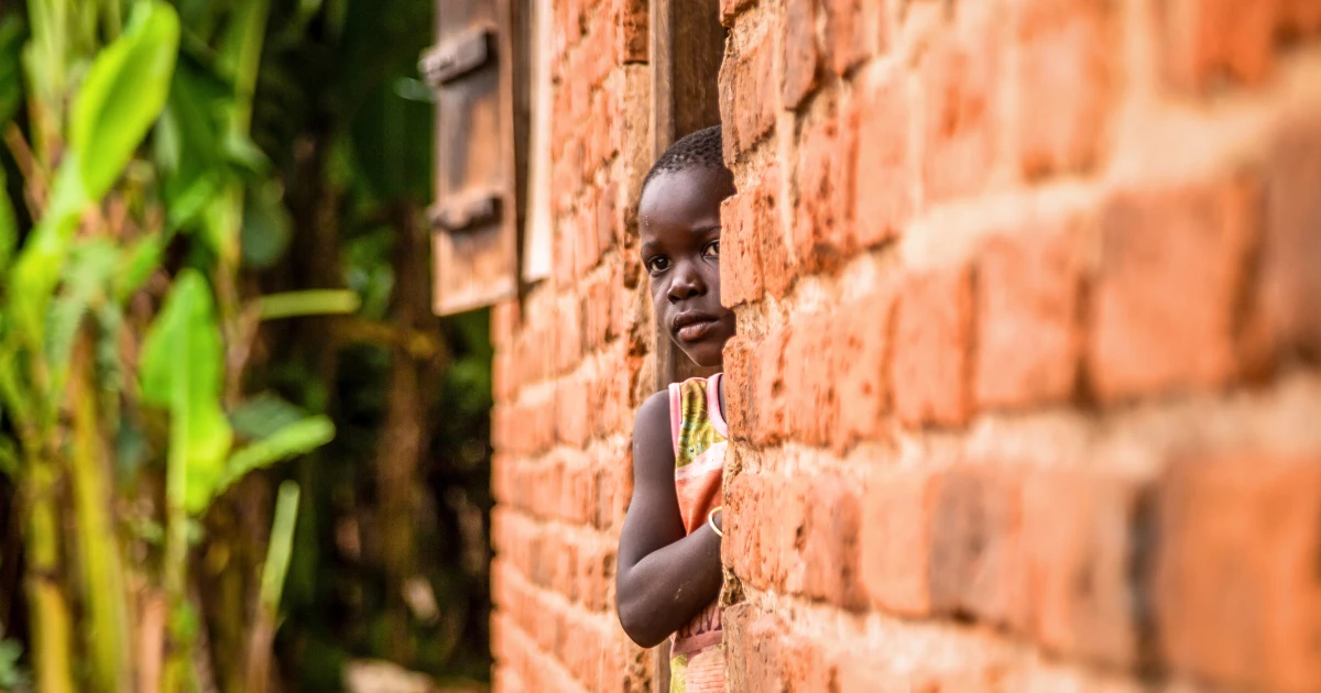 A shy young Ugandan girl stands quietly by the entrance to her house. There are countless children who still dream of going to school. This image encapsulates the mission of Baino Social Impact: to combat poverty and illiteracy in rural Africa by providing education and hope.