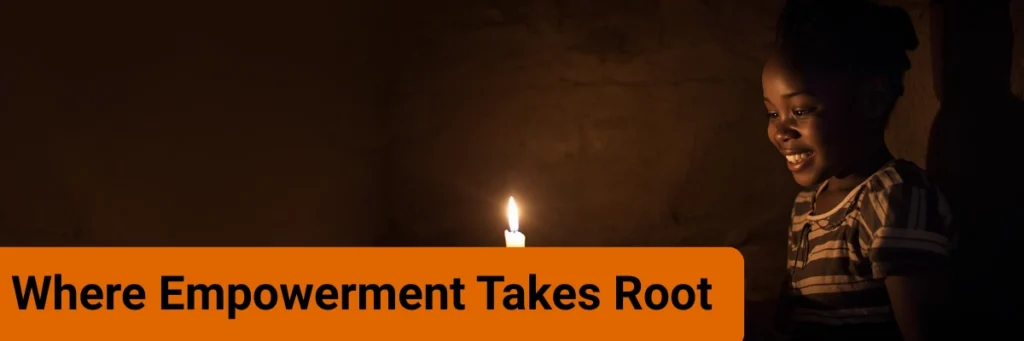 A young rural girl smiles as she reads her books by the light of a candle. The image symbolizes where empowerment takes root, showing how Baino Social Impact nurtures curiosity, education, and self-determination even in challenging circumstances.