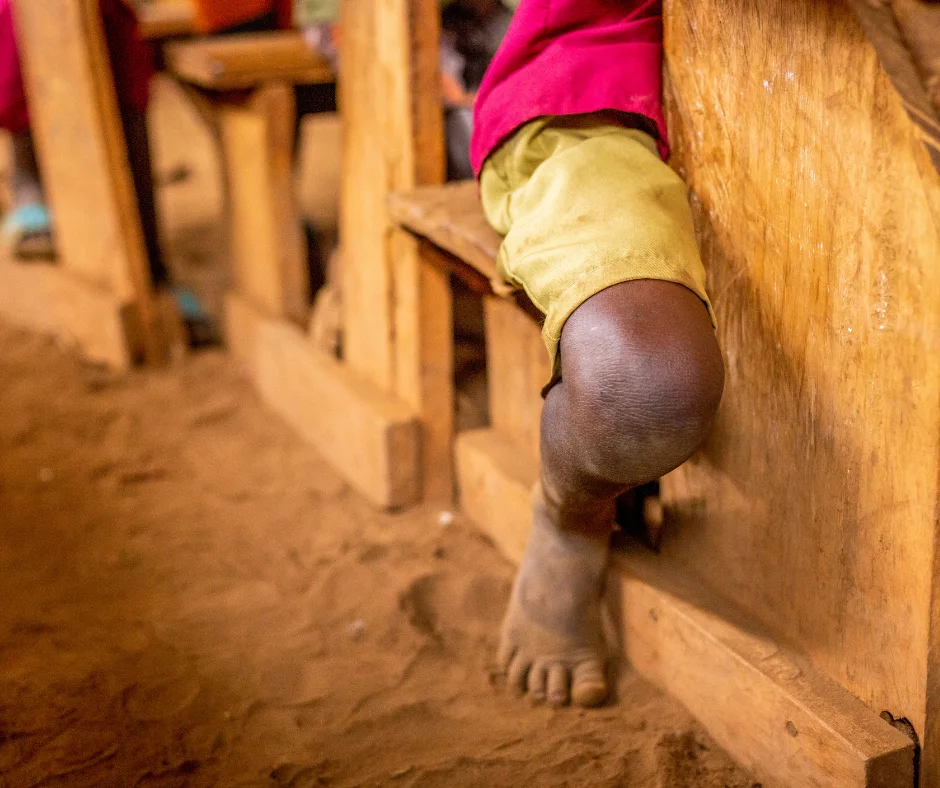 Barefoot Ugandan boy sits at a desk in an unfinished rural classroom—reflecting the resilience of children learning in harsh conditions and Baino Social Impact’s mission to build schools worthy of their potential.
