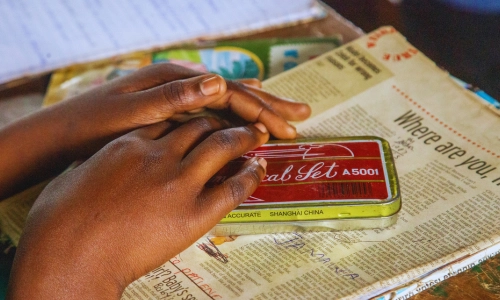 The hands of a young Ugandan girl rest gently on her geometry set placed over an open notebook inside a classroom. The quiet focus of the moment reflects the power of education to open new worlds and the promise that Baino Social Impact works to protect for every child.