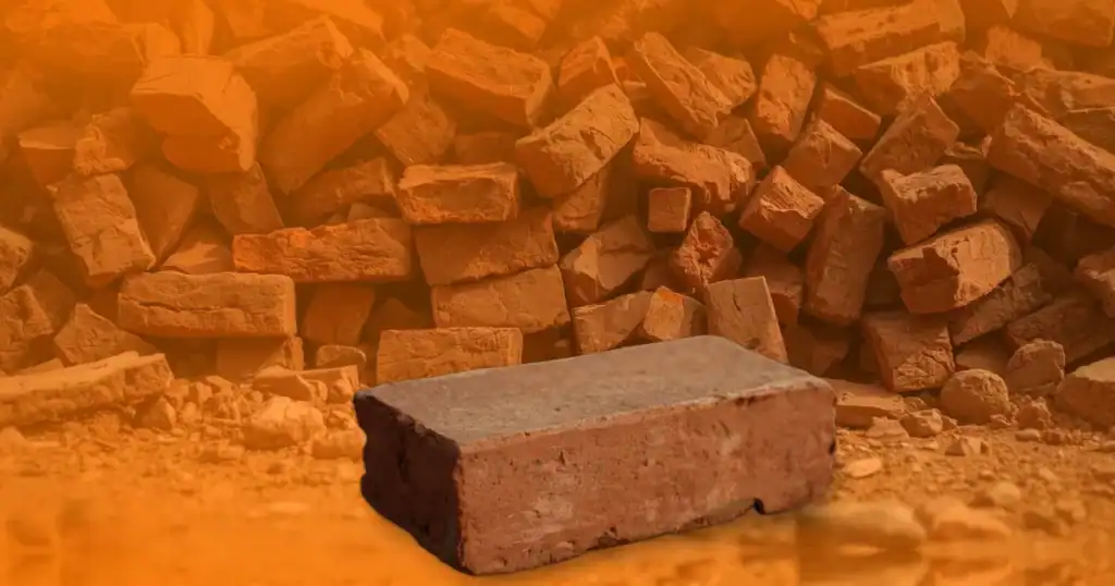 Close-up of a single clay brick with a heap of bricks blurred in the background, softly covered by Baino Social Impact’s orange gradient — symbolizing readiness, empowerment, and the ongoing work of building futures that last beyond handouts.