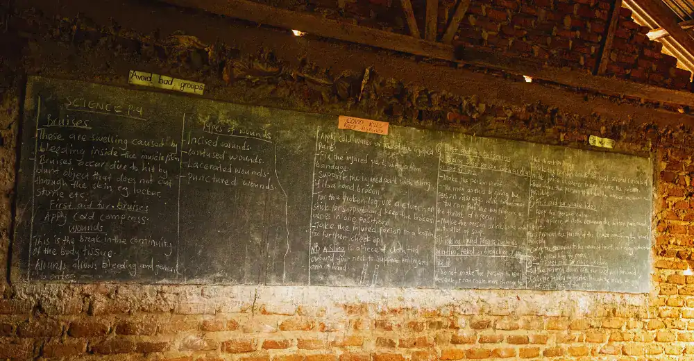 A large blackboard stands at the center of an unfinished classroom wall in rural Uganda — a quiet symbol of learning taking shape and the promise of education rising, brick by brick, through Baino Social Impact.