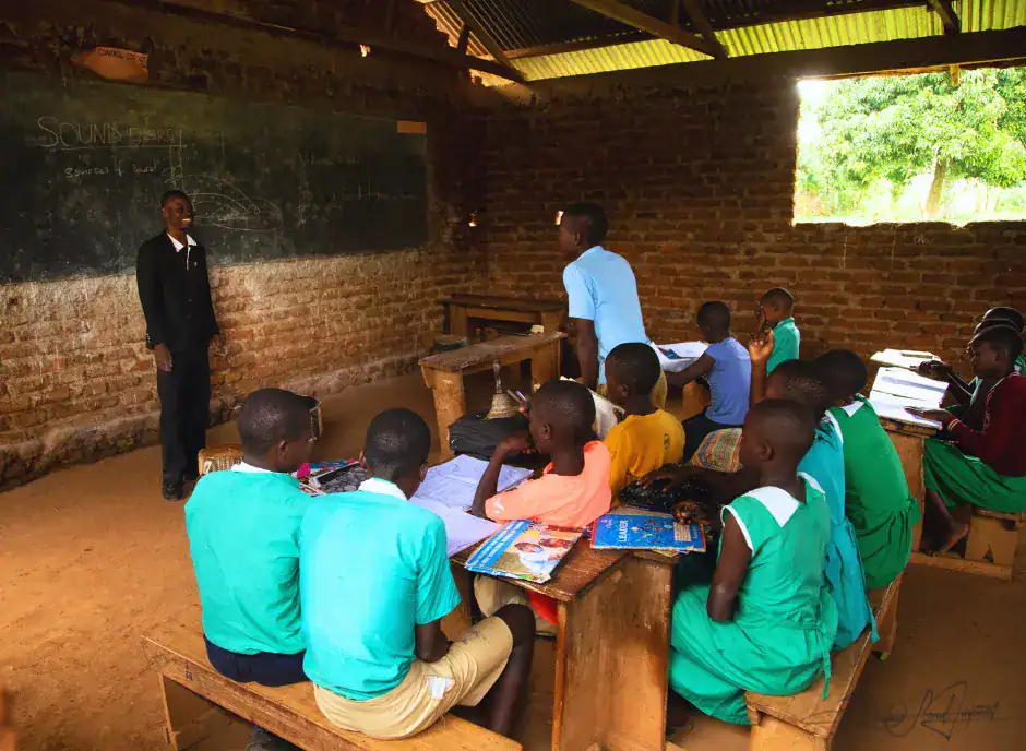A dedicated teacher guides young students inside an unfinished classroom in rural Uganda — a vivid portrait of learning taking root amid scarcity, and of Baino Social Impact’s mission to turn incomplete walls into spaces of hope and opportunity.